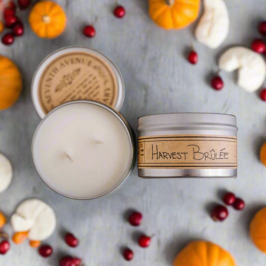 Candle with 'Harvest Brèlé' label surrounded by pumpkins and berries on a gray surface