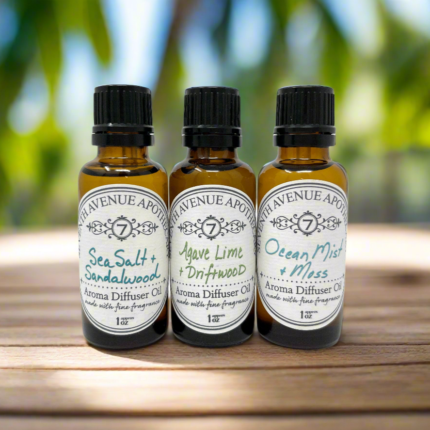 Three small dark glass bottles with white labels, containing different aroma oils. The labels indicate 'Sea Salt + Sandalwood', 'Agave Lime + Driftwood', and 'Ocean Mist + Moss'.