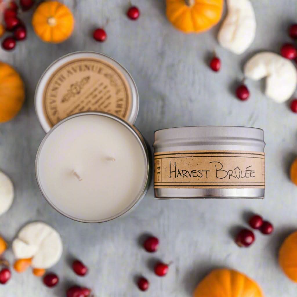 Candle with 'Harvest Brèlé' label surrounded by pumpkins and berries on a gray surface